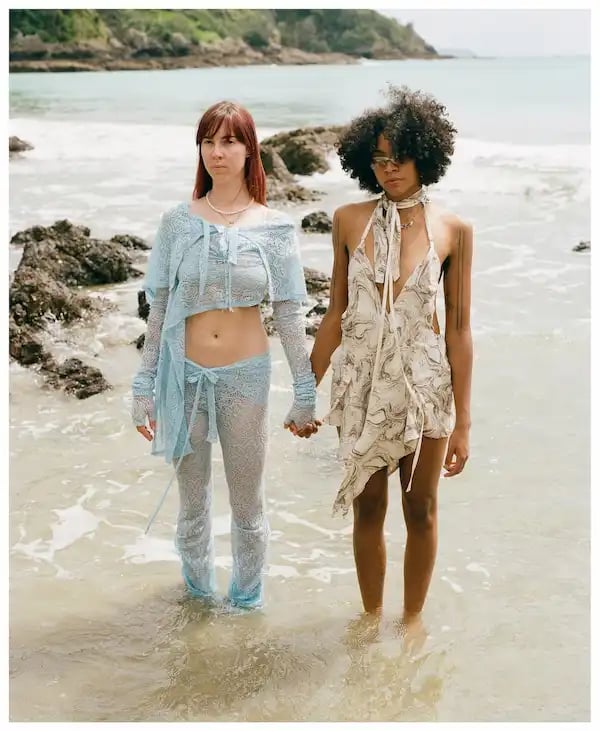 Kédu Carlö in the ocean, ankle-depth on an island holding hands.